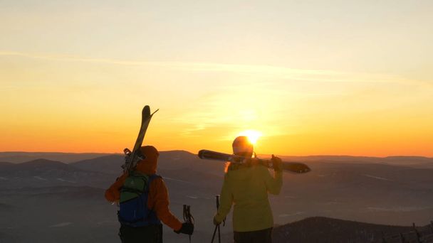 Group of friends with ski and snowboards walking against sunset - Photo, Image