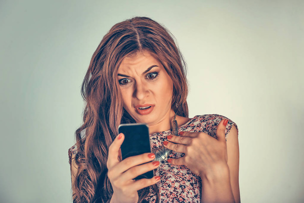 Woman looking at her phone with shocked, disgusted expression on face. Mixed race model isolated on light green background with copy space. Horizontal image. - Zdjęcie, obraz