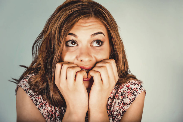Closeup portrait headshot nervous stressed young woman girl employee student biting fingernails looking anxiously craving something isolated grey wall background. Human emotion face expression feeling - Foto, immagini