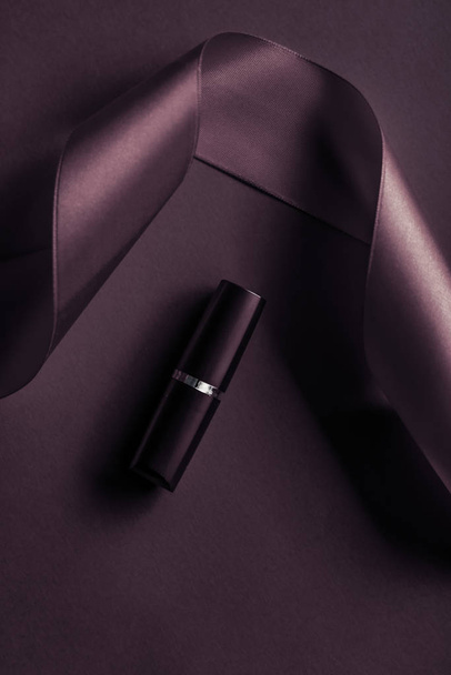 Lápiz labial de lujo y cinta de seda en el fondo de vacaciones púrpura oscuro
 - Foto, Imagen