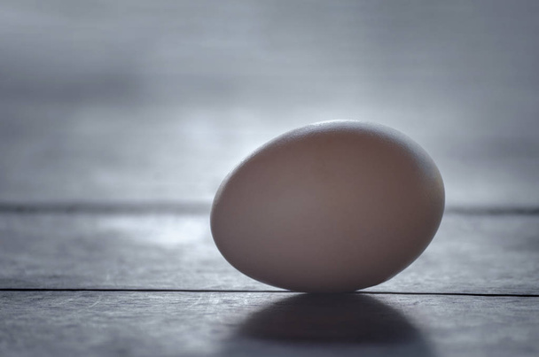 Закрыть куриное яйцо, изолированное на деревянном столе на темном фоне
 - Фото, изображение