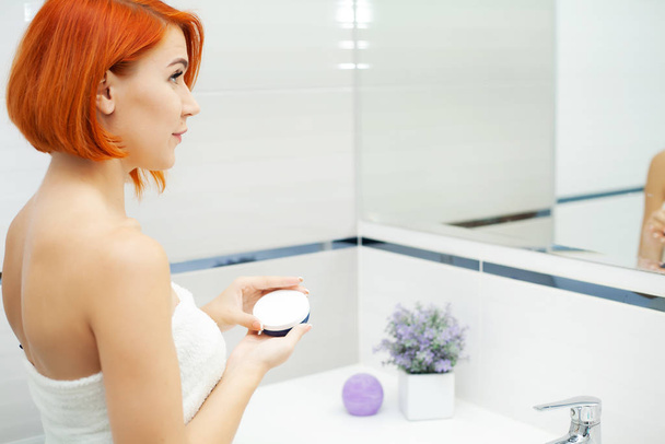 バスルームで赤い髪の女性はケア製品を使用します - 写真・画像