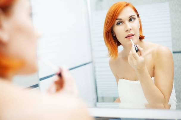 Nainen, jolla on punaiset hiukset kylpyhuoneessa käyttää hoitotuotteita
 - Valokuva, kuva
