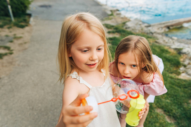 Две забавные девушки играют с мыльными пузырями на улице, дети веселятся вместе
 - Фото, изображение