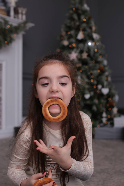 Joven hermosa chica con el pelo largo y oscuro está jugando con galletas en las luces bokeh de Año Nuevo en un árbol de Navidad decorado
 - Foto, Imagen