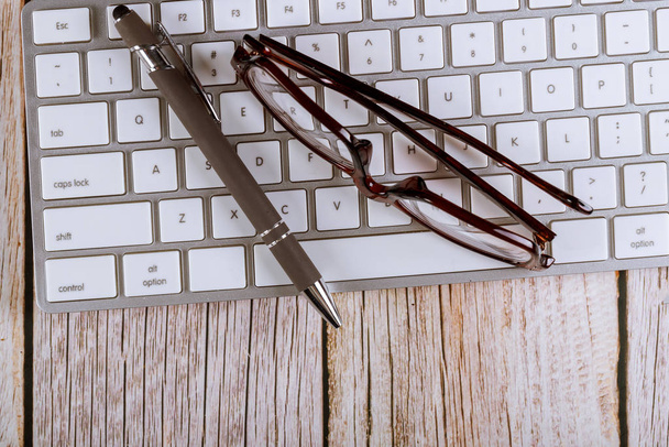 Detailní záběr brýlí na čtení a pera na klávesnici počítače kancelářský stůl - Fotografie, Obrázek
