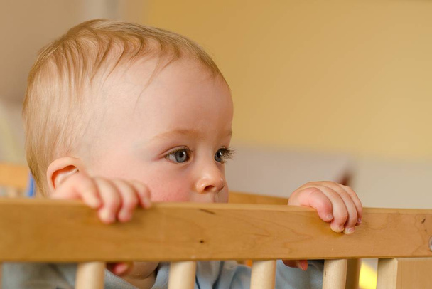 Closeup portrait of lonely toddler bites wooden bed frame.  - Photo, Image