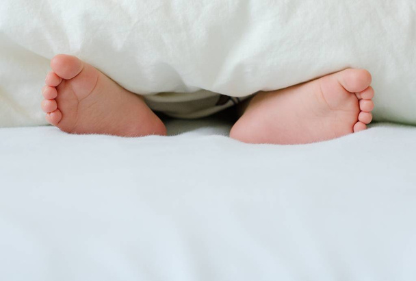 Cute foot of sleeping baby poking of a white blanket.  - Photo, Image