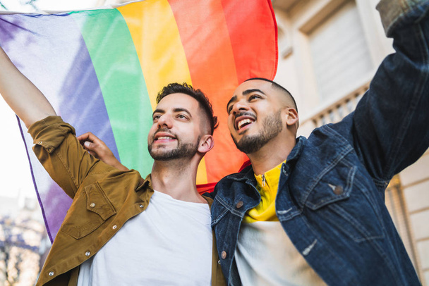 Gay couple embracing and showing their love with rainbow flag. - Foto, immagini