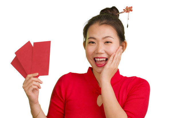 young beautiful and happy Asian Chinese woman in traditional New Year red dress and hair bun holding red pocket envelopes containing money as blessing from friends and family - Fotó, kép