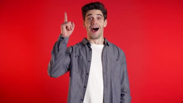 Portrait of young thinking pondering man having idea moment pointing finger up on red studio background. Smiling happy student guy showing eureka gesture. - Metraje, vídeo
