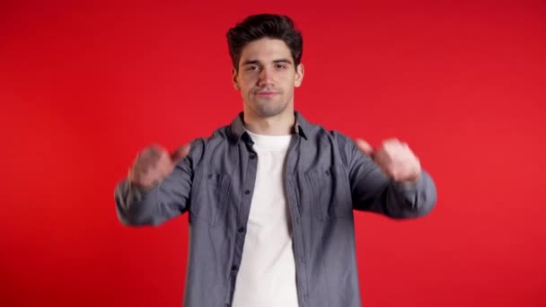 Young handsome man standing on red studio background expressing discontent and showing thumb down gesture at camera. Portrait of guy with sign of dislike. - Metraje, vídeo