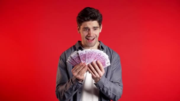 Man in denim shirt with surprised happy face holding US currency. Person with money. New dollars in hands on red studio background . - Filmagem, Vídeo