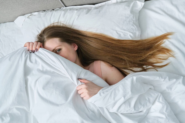 Tvář mladé krásné ženy ležící na polštáři v posteli s dekou - Fotografie, Obrázek