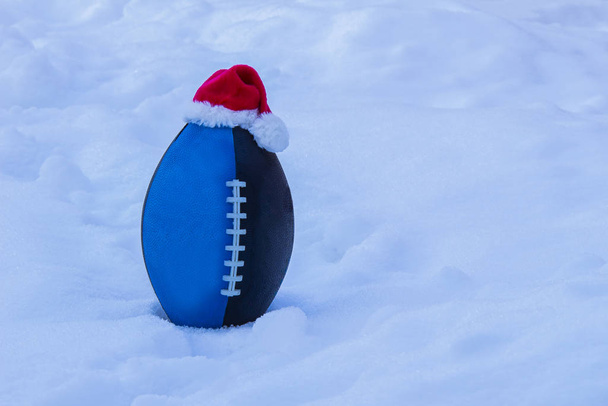 Μπλε μαύρο ποδόσφαιρο Τζούνιορ φορώντας ένα καπέλο του Αϊ Βασίλη στο χιόνι - Φωτογραφία, εικόνα