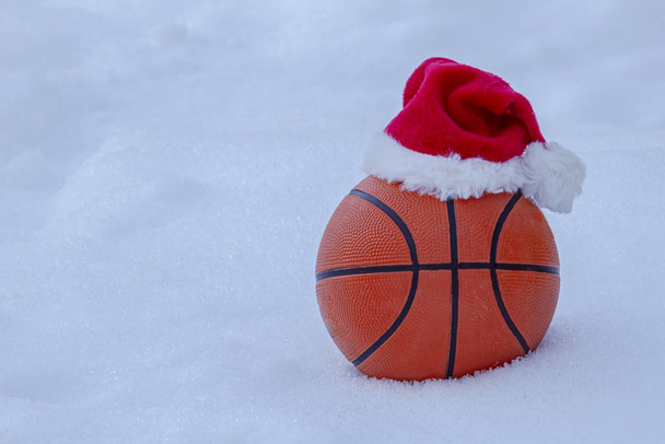 Basket ball portant un chapeau de Père Noël sur la neige pendant l'hiver
 - Photo, image