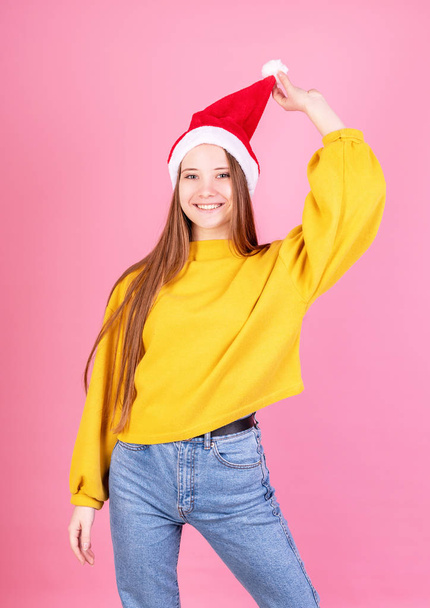 Joven mujer riendo en sombrero de santa y suéter amarillo sobre fondo rosa
 - Foto, imagen