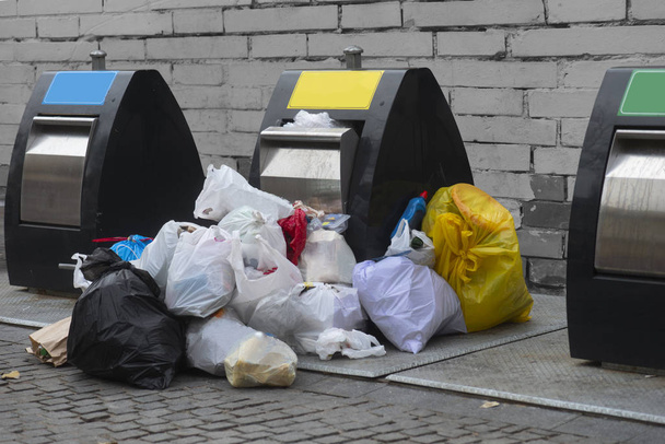 Сміттєві баки на вулиці з безліччю пластикових мішків для сміття на тротуарі
 - Фото, зображення