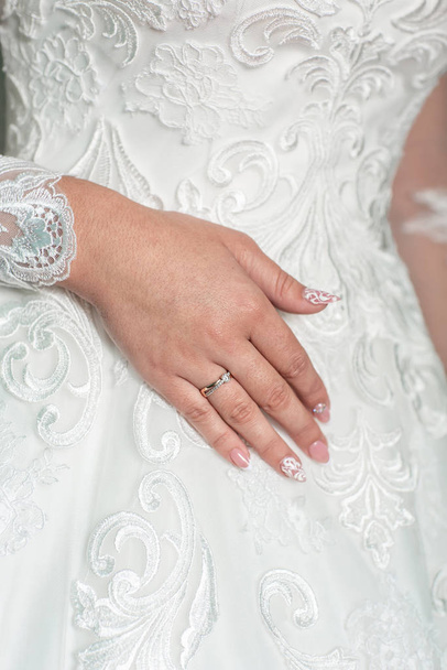 Τα χέρια της νύφης αγγίζουν το νυφικό. Φόρεμα γάμου σε κούκλα. Το χέρι της νύφης αγγίζει τη δαντέλα. Κλείσε. Το χέρι της νύφης είναι ντυμένο.Η νύφη παίρνει ένα λευκό νυφικό - Φωτογραφία, εικόνα
