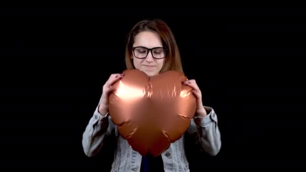 Een boze jonge vrouw scheurde een ballon in de vorm van een hart. Boze vrouw op een zwarte achtergrond. Valentijnsdag is de dag van alle minnaars. - Video