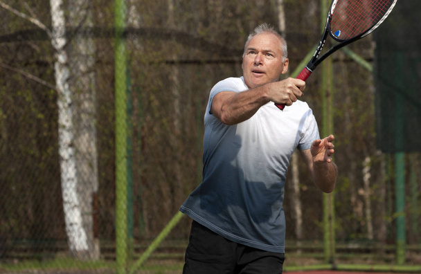 Чоловік грає в теніс на відкритому корті
 - Фото, зображення