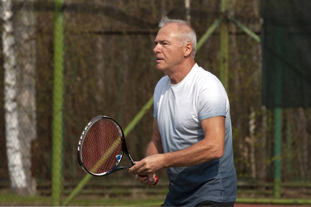 Mies pelaa tennistä ulkona kentällä
 - Valokuva, kuva