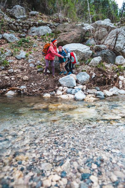 Una mujer con dos hijos camina por un río de montaña
.  - Foto, imagen