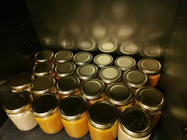 Allineamento di piccoli vasi di vetro vuoti con tappi in metallo dorato di marmellata fatta in casa su sfondo nero con riflessi di luce
 - Foto, immagini