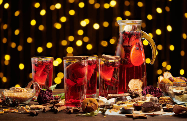 Christmas mulled wine or gluhwein with spices, chocolate sweets and orange slices on rustic table, traditional drink on winter holiday, christmas lights and decorations - Foto, imagen