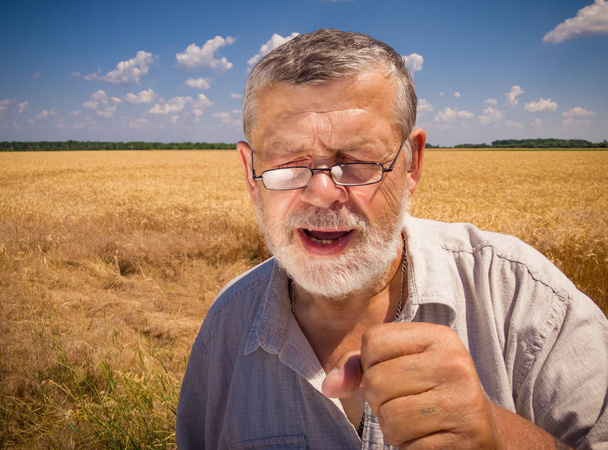 Retrato ao ar livre de fazendeiro sênior caucasiano cantando como em karaoke enquanto estava contra o campo de trigo na temporada de verão
 - Foto, Imagem