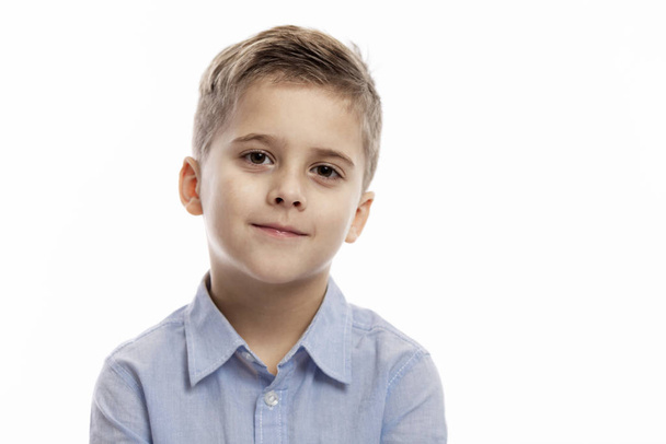 Cute smiling boy in a blue shirt is looking at the camera. White background. Close-up. - Φωτογραφία, εικόνα