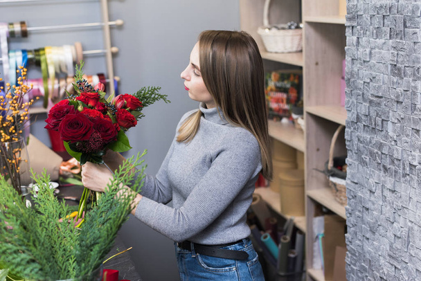 Güzel bir kız stüdyosunda koyu kırmızı güller topluyor. Erkek çiçekçi çiçekçide güzel bir buket yapıyor. Çiçek teslimatı, düzen yaratmak, küçük işletmeler.. - Fotoğraf, Görsel