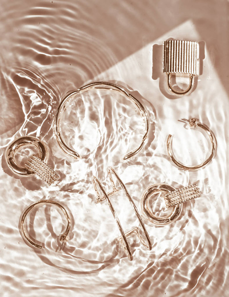 Bracelets dorés, boucles d'oreilles, bagues, bijoux sur l'eau dorée backgr
 - Photo, image
