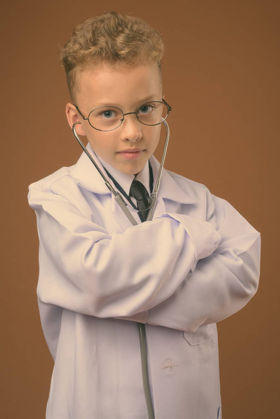 Studio shot of young boy as doctor against brown background - Foto, immagini