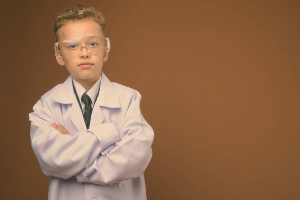 Studio shot of young boy as doctor against brown background - Photo, Image