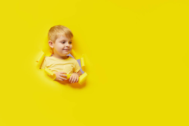 Little surprised child looking, peeping through the bright yellow paper hole. Advertise childrens goods. Happy childhood concept. Copy space for text	 - Foto, imagen