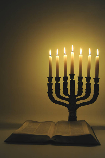 Menorah και ανοιχτή Αγία Γραφή με 7 αναμμένα κεριά που απομονώνονται σε χρυσό φόντο. Κάθετη βολή. - Φωτογραφία, εικόνα
