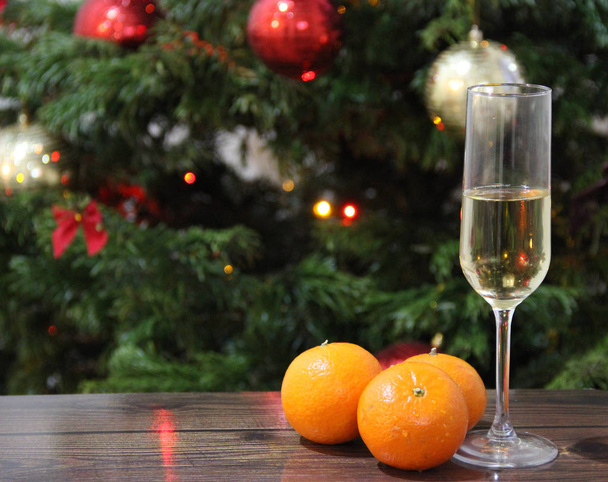Champagnerglas und Mandarinen neben den flackernden Lichtern des Weihnachtsbaums - Foto, Bild