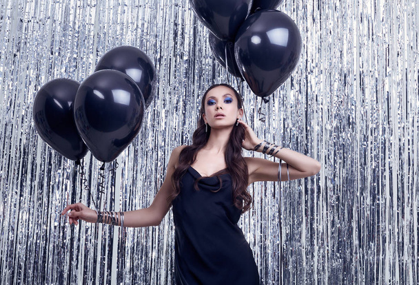 Elegante latino brunette vrouw in luxe zwarte jurk houdt ballonnen - Foto, afbeelding