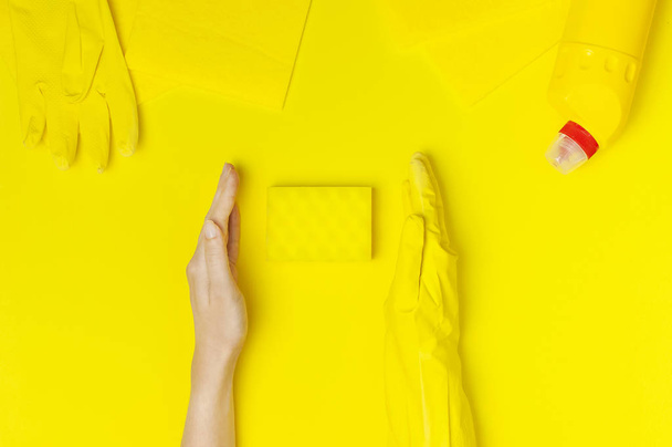 House cleaning concept. Women's hands in yellow rubber gloves, household chemicals, bleach, antibacterial gel, sponge, rags on yellow background. Flat lay top view copy space. Cleaning accessories - Foto, afbeelding