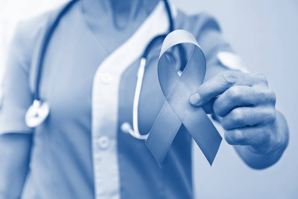 Médica de uniforme feminina segura fita azul na mão como campanha de conscientização sobre câncer de próstata em novembro
 - Foto, Imagem