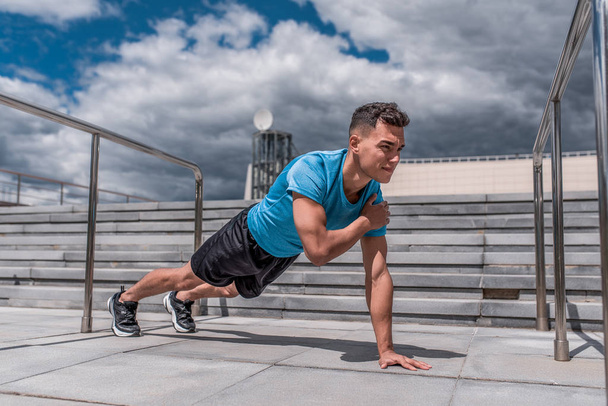Young sportsman, male athlete, push ups in the bar, in the summer in the city, workout fitness training, active lifestyle of modern youth, sportswear t-shirt shorts sneakers. Motivation for life. - Fotoğraf, Görsel