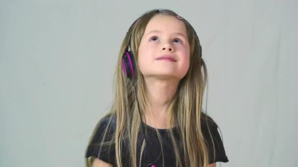 Όμορφο χαμογελαστό κορίτσι που ακούει μουσική με μεγάλα ροζ ακουστικά. - Πλάνα, βίντεο