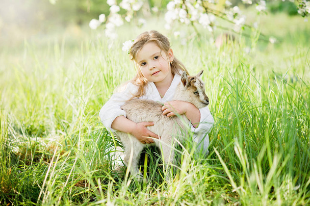 Κορίτσι με κατσικάκι. Φιλία παιδιών και ζώων. Χαρούμενη παιδική ηλικία. - Φωτογραφία, εικόνα