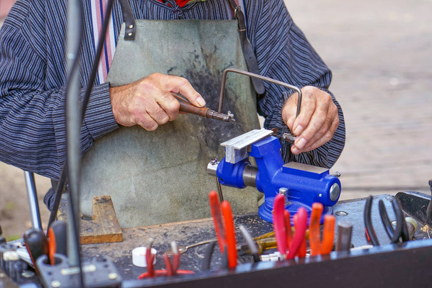Пожилой человек работает в мастерской на улице
. - Фото, изображение