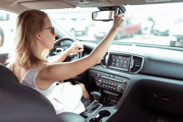 woman in car, adjusts and rearview mirror, driving safety in car, parking and rear traffic. Reverse parking in car. In summer in city, a pink dress. Automatic transmission. - Foto, imagen