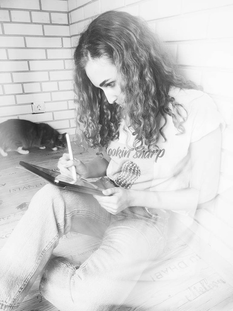 Kıvırcık kadın duvarın yanında oturuyor ve tablet kullanıyor - Fotoğraf, Görsel