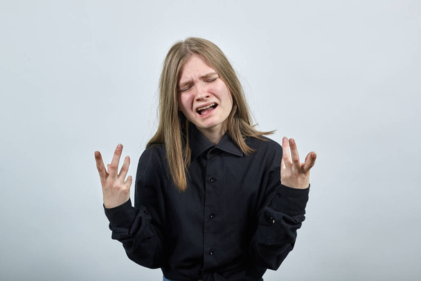 unglückliche kaukasische junge Frau im modischen schwarzen Hemd breitet weinend die Hände aus. - Foto, Bild