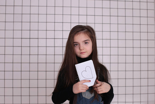 jeune fille souriante de huit ans avec les cheveux longs dans un col roulé noir et robe de soleil en denim avec un signe "amour et coeur
" - Photo, image