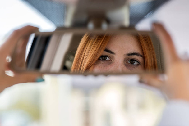 Νεαρή γυναίκα οδηγός ελέγχει τον καθρέφτη οδήγησης κοιτάζοντας προς τα πίσω - Φωτογραφία, εικόνα